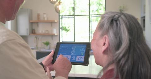 Mature couple controlling smart home with tablet in bright modern kitchen daylight airy