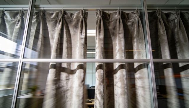 Closing heavy velvet curtains across office glass partition with reflective metal frames