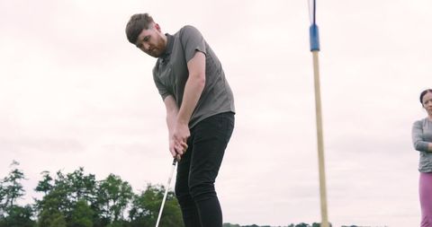 Couple enjoying golf, man practicing putting on green