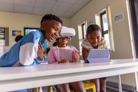 African american children using vr headset and tablet in classroom learning together
