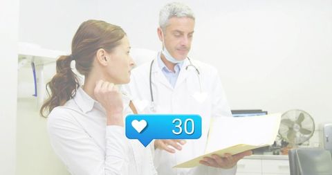 Doctor consulting female patient reviewing medical chart with social heart notification