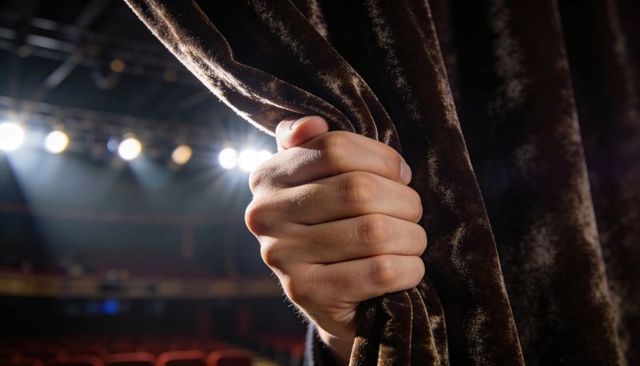 Strong Hand Pulling Velvet Curtain on Theater Stage Revealing Spotlight and Auditorium