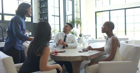 Modern team mingling around wooden dining table in bright open kitchen for casual networking