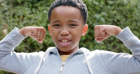 African american boy flexing muscles in gray hoodie and yellow tee, confident playful youth