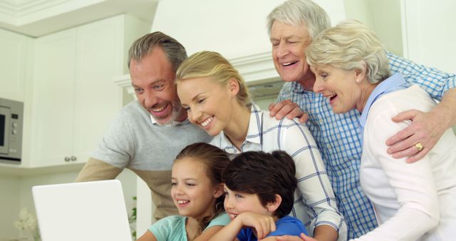 Multigenerational family gathering together smiling while looking at laptop in the comfort of their home. Useful for depicting family bonds, technology use across generations, happy moments at home, or family-friendly technology marketing.