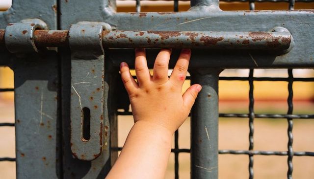 Toddler grasping rusted gate bar close-up small hand holding metal fence latch texture