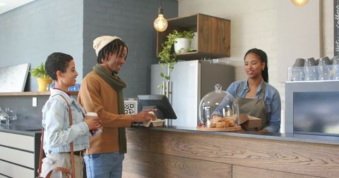 Young couple ordering coffee and pastries using contactless payment at modern cafe counter