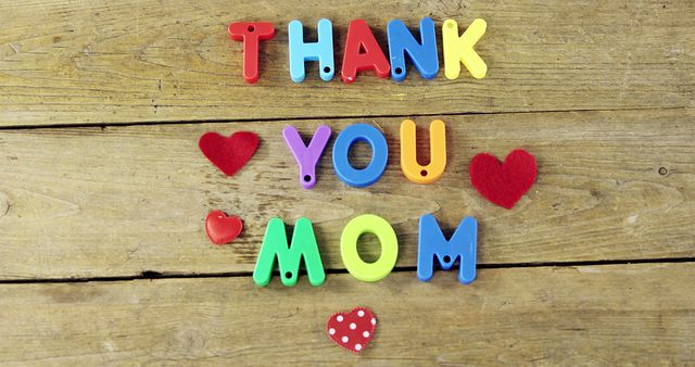Colorful plastic letters spelling 'Thank You Mom' with hearts on wooden background. Suitable for Mother's Day cards, appreciation messages, gifts for mom, social media posts celebrating mothers, and blog posts dedicated to mother's love.