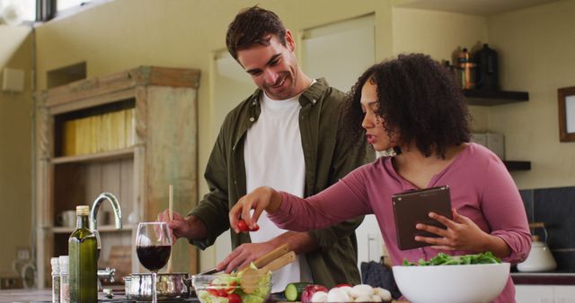 Happy diverse couple preparing a meal together in kitchen, using recipe on tablet. spending free time together at home.