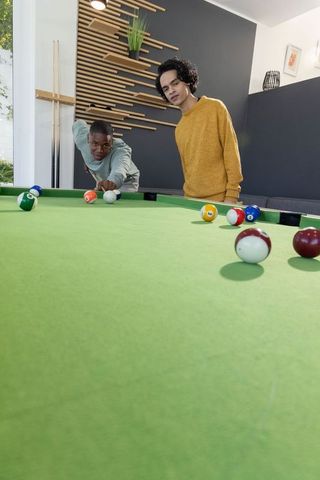 Two friends playing pool on green felt table in modern lounge