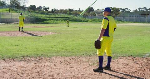 Sunlit baseball teammates standing on diamond in bright yellow uniforms holding gloves