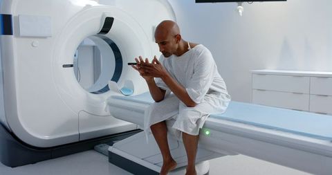 Male patient sitting on ct scanner table holding smartphone in modern radiology clinic