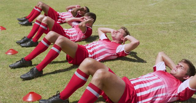 Diverse male football team exercising on sunny sports field doing sit ups. Training, fitness, sport, team sport and competition, unaltered.