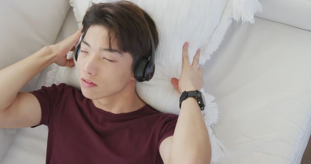 Asian male teenager listening to music with headphones in living room. spending time alone at home.