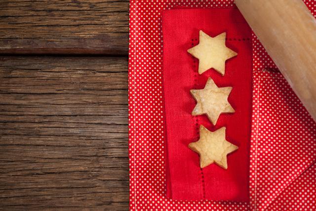 This image shows three star-shaped cookies placed on a red napkin with a rolling pin nearby, set on a wooden table. Ideal for use in holiday baking articles, Christmas recipe blogs, festive greeting cards, or advertisements for baking supplies and kitchenware.