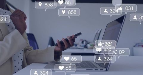 Businesswoman checking smartphone while working on laptop with social media notifications