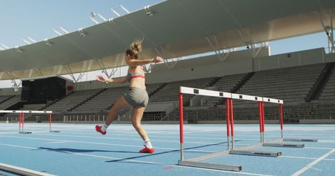 Female Athlete Clearing Hurdle on Track with Determination
