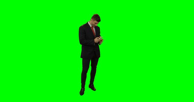 Man wearing a suit standing isolated against a green screen background, focusing on his phone. Ideal for businesses needing a professional image for digital content, technology advertising, or business consultancy services.