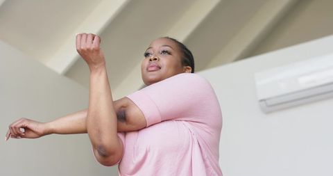 African american woman stretching arm across chest in bright room promoting wellness