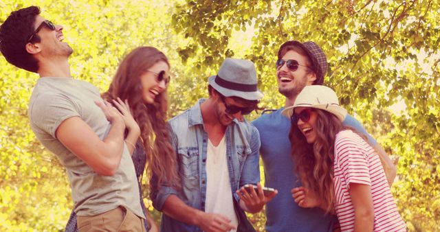 A group of young, diverse friends laugh and enjoy a sunny day outdoors, with copy space. Their casual attire and joyful expressions suggest a relaxed and happy social gathering.