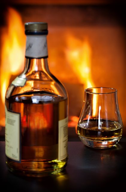 Whiskey bottle and glass in front of warm fireplace - Download Free Stock Photos Pikwizard.com