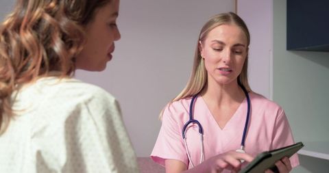 Nurse in pink scrubs tapping tablet while explaining care plan to patient in gown