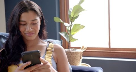 Teenage Girl Smiling Using Smartphone on Couch Near Window