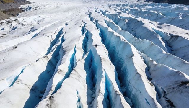 Solo hiker crossing glacier crevasse on ice ridge, aerial trekking adventure blue ice