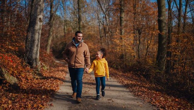Father and daughter walking hand-in-hand on sunlit autumn trail with golden leaves