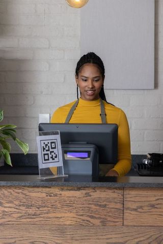 African american barista operating pos terminal at modern café counter with qr code