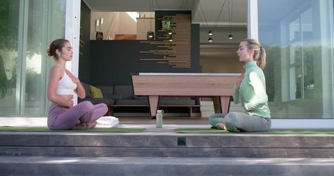 Two women practicing outdoor yoga on modern patio sharing breath and hydration