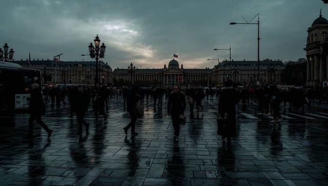 Moody urban square at dusk with walking commuters, wet reflections, silhouettes and dome
