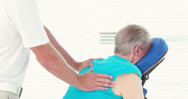 Elderly man receiving massage on portable massage chair for relaxation and pain relief. Suitable for use in articles, blogs, or advertisements related to senior health, wellness practices, and therapeutic treatments for the elderly.