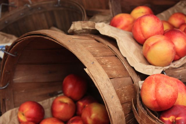 Fresh, ripe nectarines are beautifully displayed in rustic wooden baskets. This close-up capture emphasizes the vibrant colors and natural textures of the freshly harvested fruit, making it ideal for use in food blogs, agricultural promotions, or grocery store marketing materials.