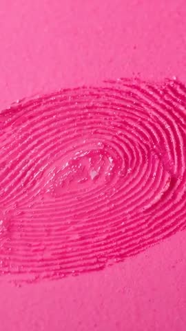 Vertical macro footage revealing glossy embossed fingerprint gel on vibrant pink paper