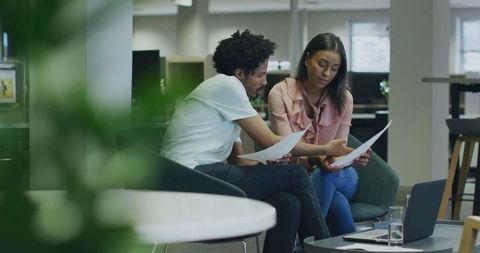 Professional colleagues analyzing documents in modern office lounge