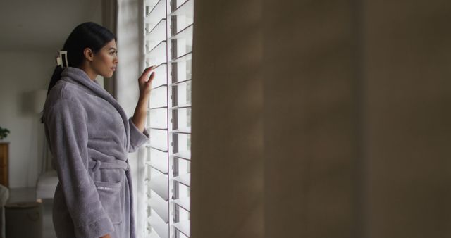 Image of biracial woman in rope looking outside window. Lifestyle, spending free time at home concept.