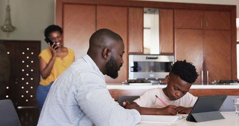 African American Father Helping Son Studying with Tablet at Kitchen Table in Modern Home