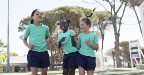 Multiracial schoolgirls skipping on sports field in mint green shirts, energetic trio