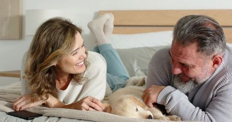 Middle-Aged Couple Relaxing on Bed with Sleeping Golden Retriever Puppy in Cozy Bedroom