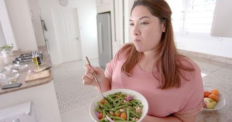 Plus Size Woman Enjoying Healthy Salad in Modern Kitchen
