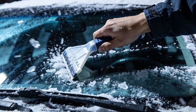 Hand scraping snow and ice from car windshield at night with ice scraper