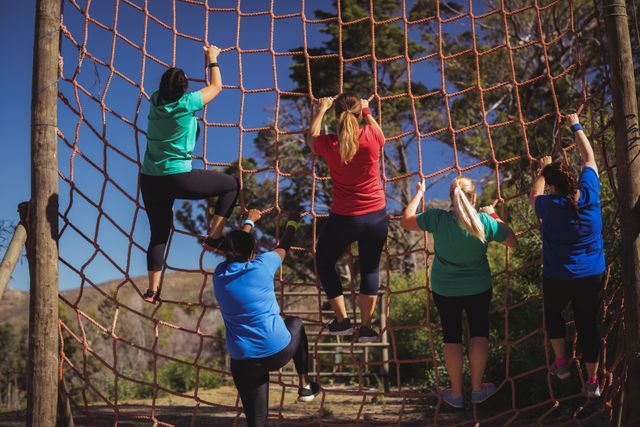 Group of women participating in an outdoor obstacle course, climbing a net together. Ideal for illustrating teamwork, fitness training, and outdoor adventure activities. Perfect for use in fitness blogs, training program advertisements, and health and wellness promotions.