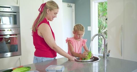 Mother and daughter rinsing lettuce at modern kitchen island sink, family cooking