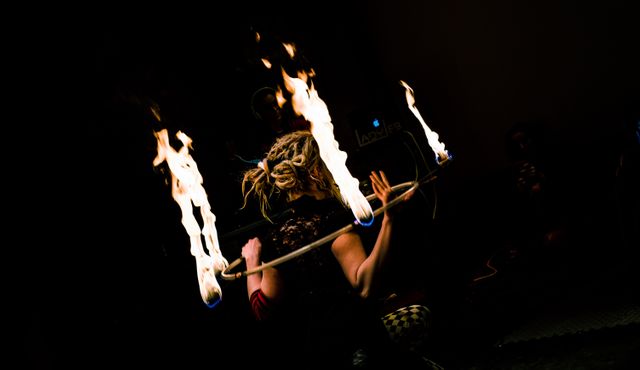 Fire performer practicing complex fire tricks at night with flaming staff. Spectacular display against dark background creates dramatic lighting. This image is ideal for promoting entertainment events, street festivals, or articles on performance arts. It also works for social media posts celebrating skilled and risky arts.