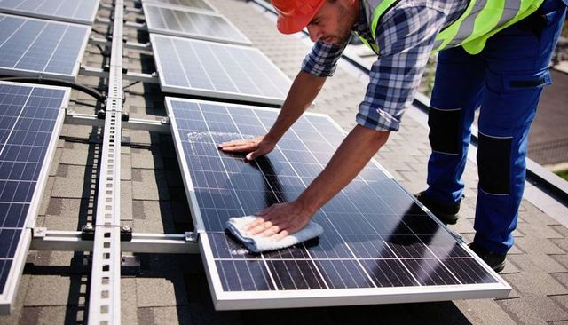 Solar Technician Cleaning Rooftop Panels Wearing High-Visibility Vest and Hard Hat