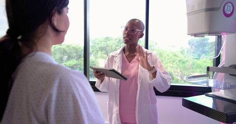 Clinician explaining mammogram to patient in breast imaging room with mammography unit
