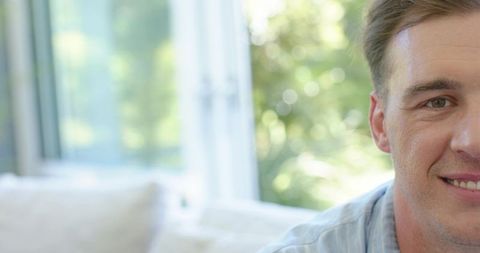 Smiling man relaxing on sofa by window with soft bokeh and natural daylight