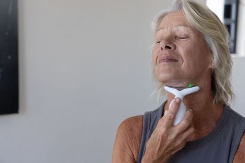 Senior woman using t-shaped led neck device for at-home facial toning and relaxation