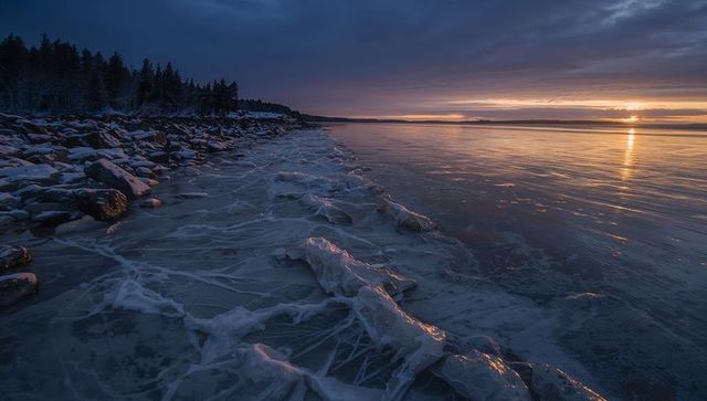 Winter Sunset Over Frozen Rocky Shoreline with Layered Ice Ridges and Golden Reflections